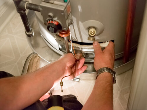 A man shines a light on the water heater.