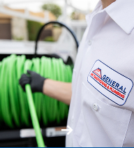 Technician holding a green hose near a service truck with plumbing equipment.