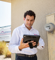 Uniformed electrician using a tablet while inspecting an outdoor electrical meter at a Palm Springs home.